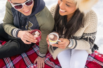 A happy couple enjoys hot chocolate on a red flannel blanket in the snow.