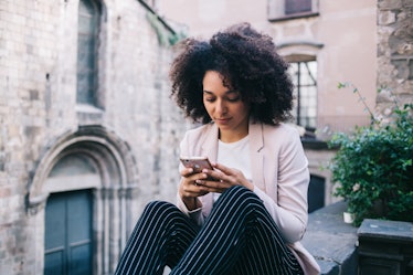 African American woman with curly hair texting in social media on smartphone while resting in Gothic...