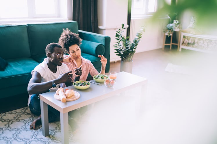 A couple hangs out in their new apartment and watches TV while eating salads.