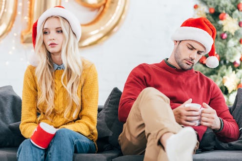 upset couple in bad mood holding cups of coffee and sitting at home on christmas eve