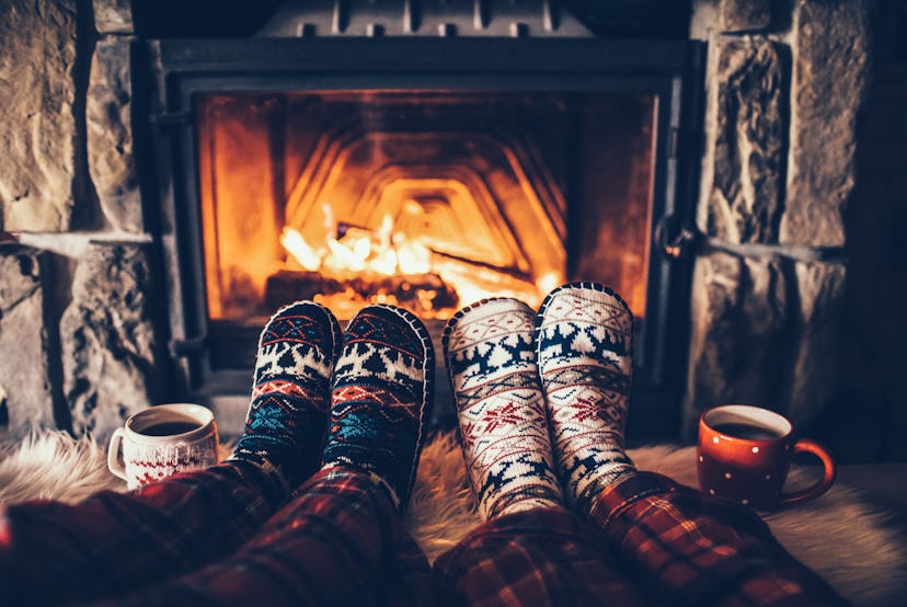 Feet in woollen socks by the Christmas fireplace. Couple sitting under the blanket, relaxes by warm ...