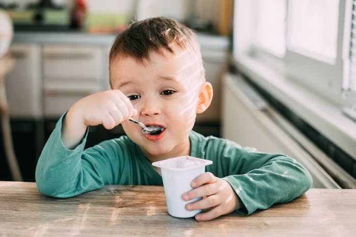 a little boy eating yogurt at a kitchen table