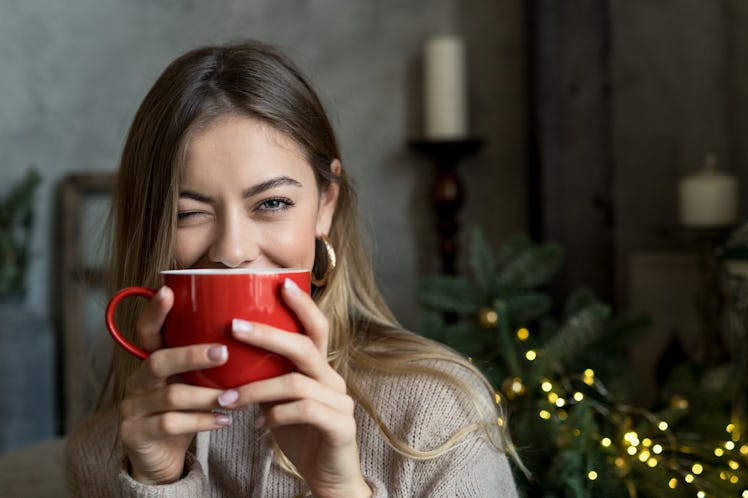 Beautiful girl drinking coffee or tea from a red cup and and winks. Christmas mood with copy space