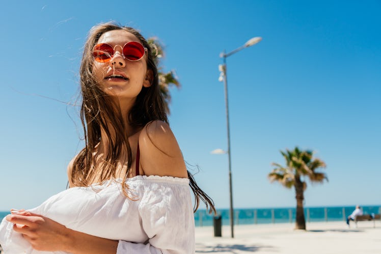 A woman in round, red sunglasses poses on the beach in Florida during Christmas.