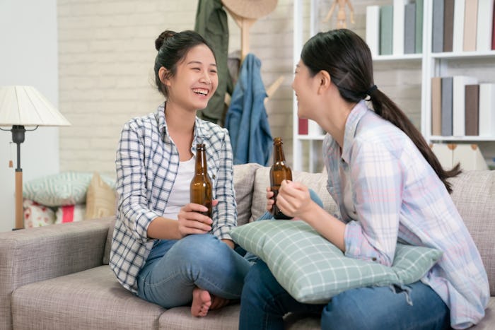 Two women hanging out on a couch, drinking beer