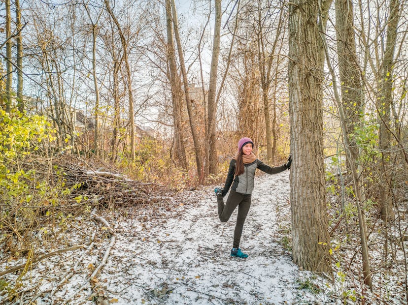 Winter running athlete woman on cold trail run getting ready stretching legs for jogging outside for...