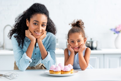 A young woman and her little cousin sit at the kitchen table with cupcakes in front of them. 