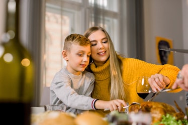 A blonde woman cuts a turkey with her little cousin at the holiday kids' table. 