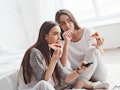 Girl licks her finger, it's so taste. Sisters eating pizza when watching TV while sits on the floor ...