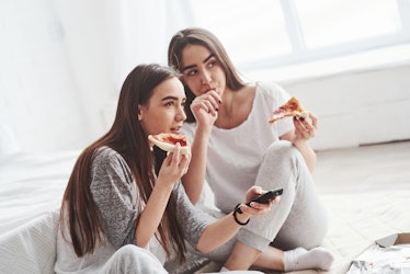 Girl licks her finger, it's so taste. Sisters eating pizza when watching TV while sits on the floor ...