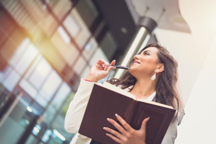 Smiling business woman standing in front of corporate building taking notes