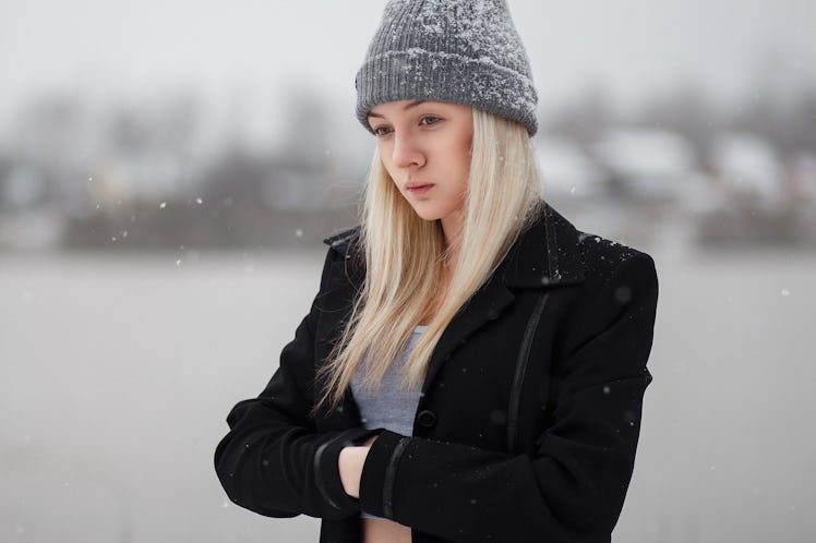 Girl winter on stroll. Girl at the frozen river. Girl in a black cloak in the snow. White snow falls...