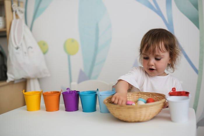 charming toddler girl sorts colorful toys by colored buckets at the table