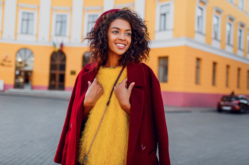 Fashionable black girl in amazing winter outfit and accessories posing on yellow background. Wavy ha...