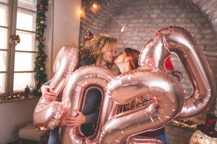 Beautiful young couple in love celebrating New Year, kissing and holding giant balloons shaped as nu...