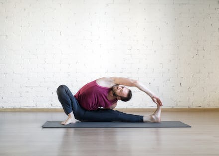 Caucasian man doing yoga, stretching on grey mat in fitness studio