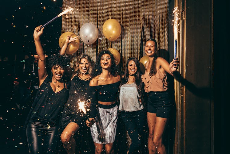 Shot best friends celebrating new year's eve holding sparklers in a party. Group of women having par...