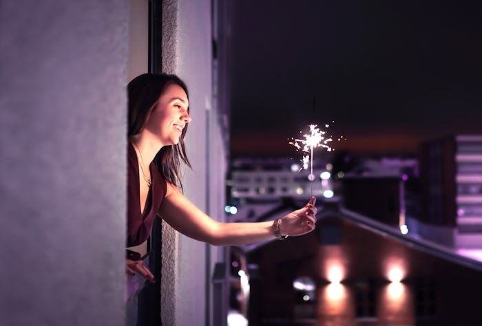 Woman holding a sparkler out of window on new year's eve 2020