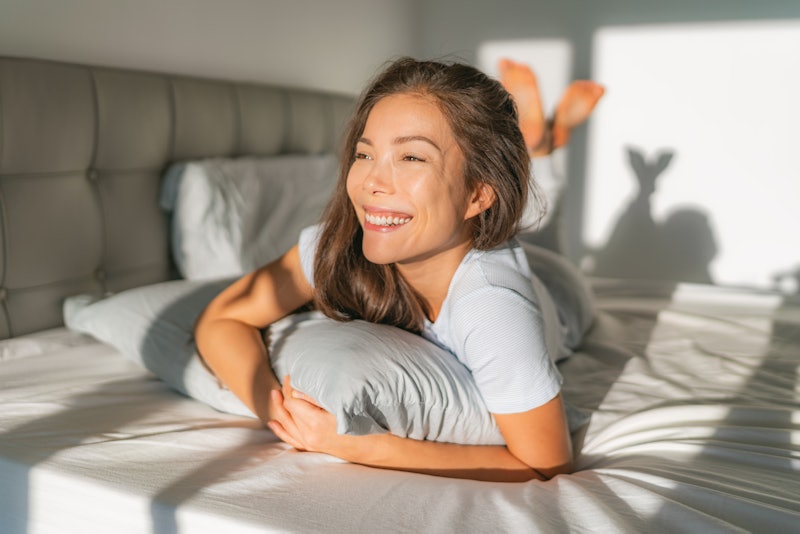 Bed woman waking up early morning happy enjoying sun on comfortable mattress and pillow. Asian girl ...