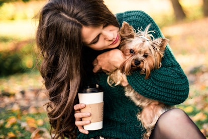 A woman walks her dog through the park with a cup of coffee in hand. 
