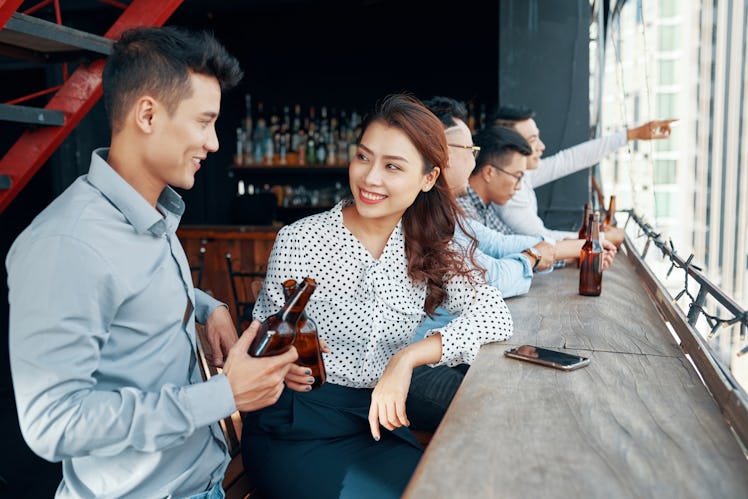 Vietnamese young man and pretty woman drinking beer and flirting in bar