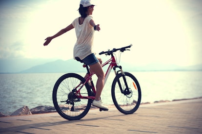 Woman riding a bike on sunny seaside with arms outstretched