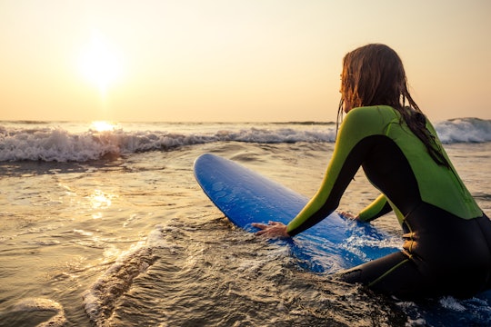 woman in a diving suit lying on a surfboard waiting for a big wave