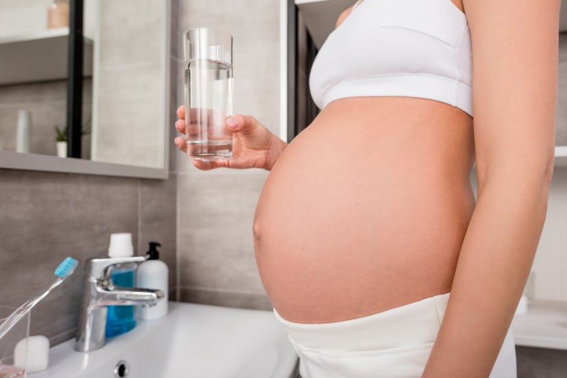 cropped shot of pregnant woman in underwear with glass of water standing in bathroom