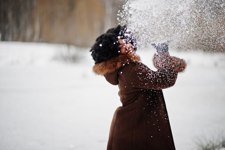 A stylish woman poses for a picture while throwing snow in the air.