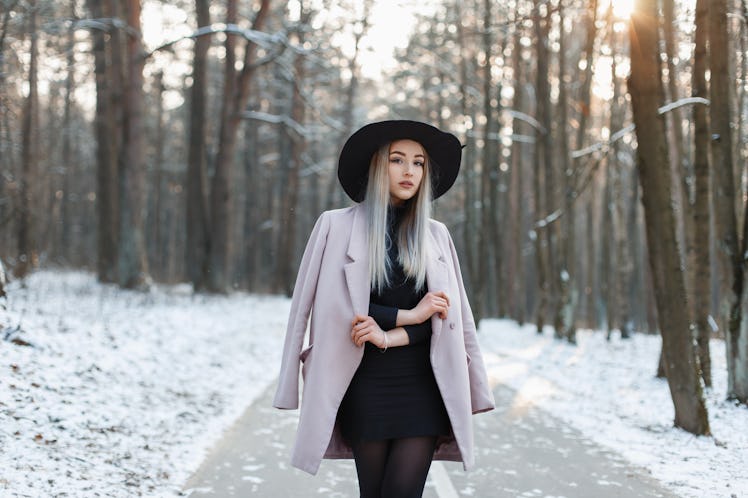 Stylish young girl walking in a winter sunny day on the background of the park with snow