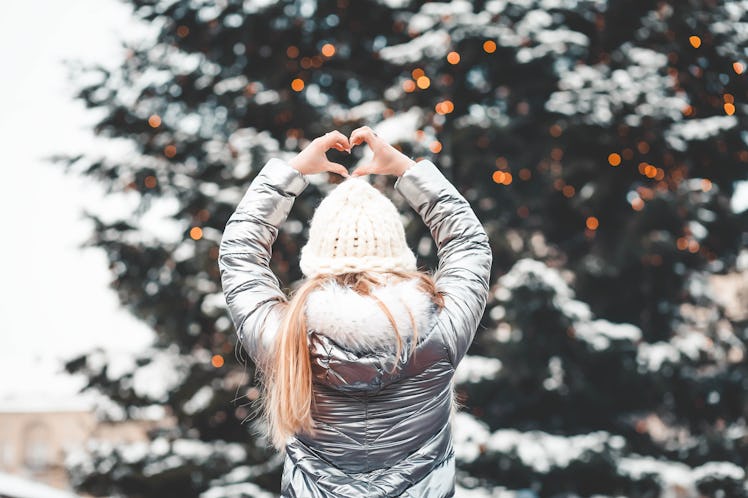 A blonde woman in a metallic jacket poses in front of a snowy, decorated Christmas tree.