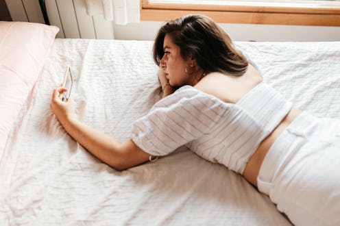 Portrait of young sad woman lying on the bed looking smartphone feels unhappy. Waiting for mobile me...