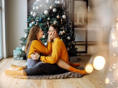 A happy couple dressed in matching yellow sweaters in front of their Christmas tree, in need of Chri...