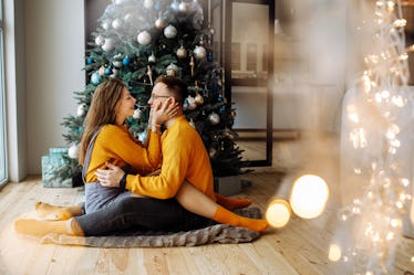 A happy couple dressed in matching yellow sweaters in front of their Christmas tree, in need of Chri...