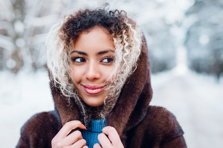 A woman smiles and looks to the side while she holds her hood up outside with snow in the background...