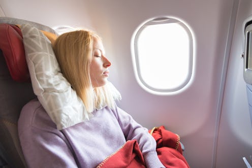 Tired blonde casual caucasian woman sleeping on seat while traveling by airplane on long distance tr...