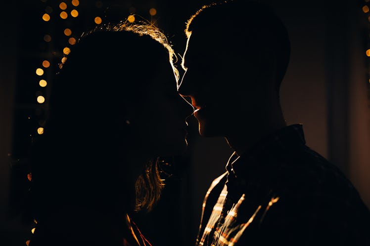 silhouette of a man and a woman on a background of lights in the dark, contour of the face, a kissin...