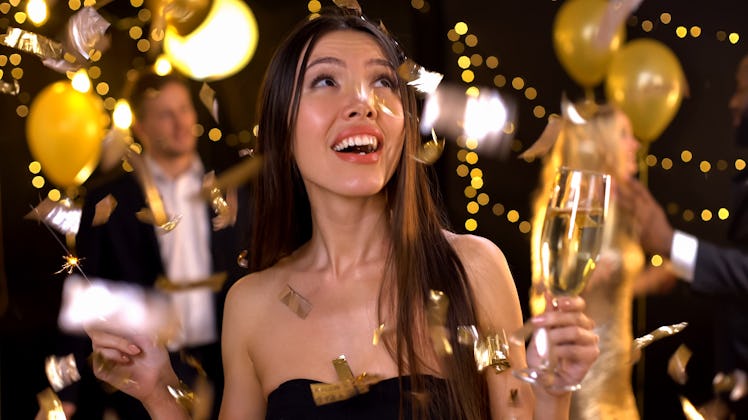 Positive woman holding champagne glass and sparkler, confetti falling down