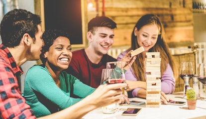 Young friends playing board games at hostel living room - Diverse culture people having fun and drin...