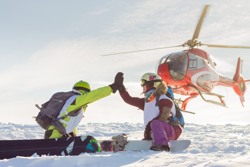 pair of freeriders of snowboarders give five when the helicopter lands