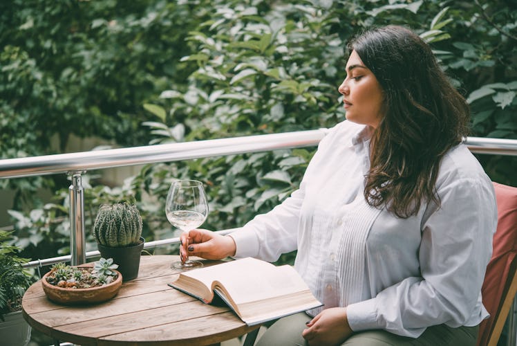 Portrait of beautiful plus size girl reading a book on balcony or terrace of cafe. Toned picture
