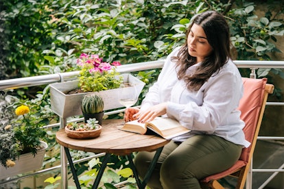 Portrait of beautiful plus size girl reading a book on balcony or terrace of cafe