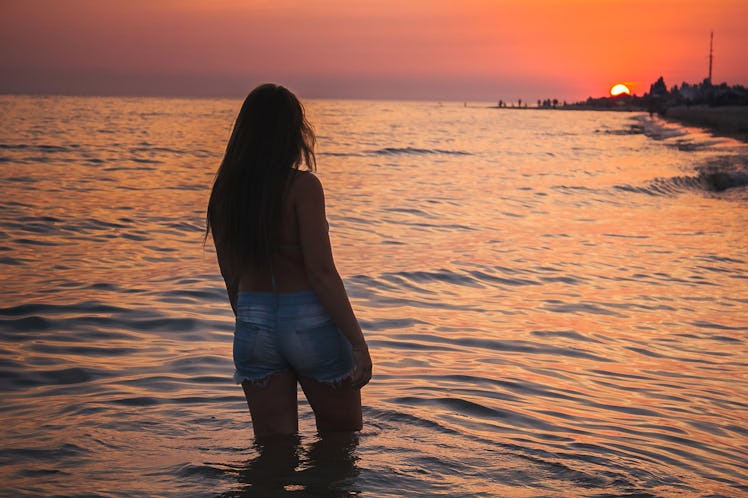 girl on a sunset background. girl and the sea. stands with his back to the sea. beautiful landscape.
