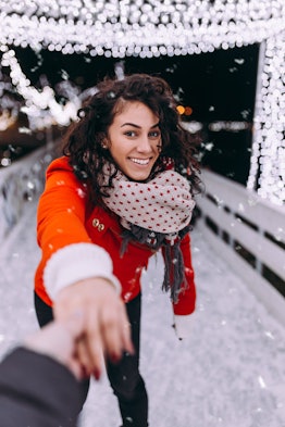 A woman holds her significant other's hand while ice skating at a rooftop ice skating rink.