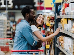 selective focus of cheerful african american man standing with asian woman smiling near groceries in...