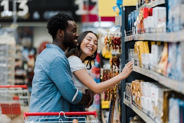 selective focus of cheerful african american man standing with asian woman smiling near groceries in...