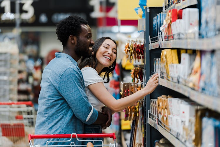 selective focus of cheerful african american man standing with asian woman smiling near groceries in...