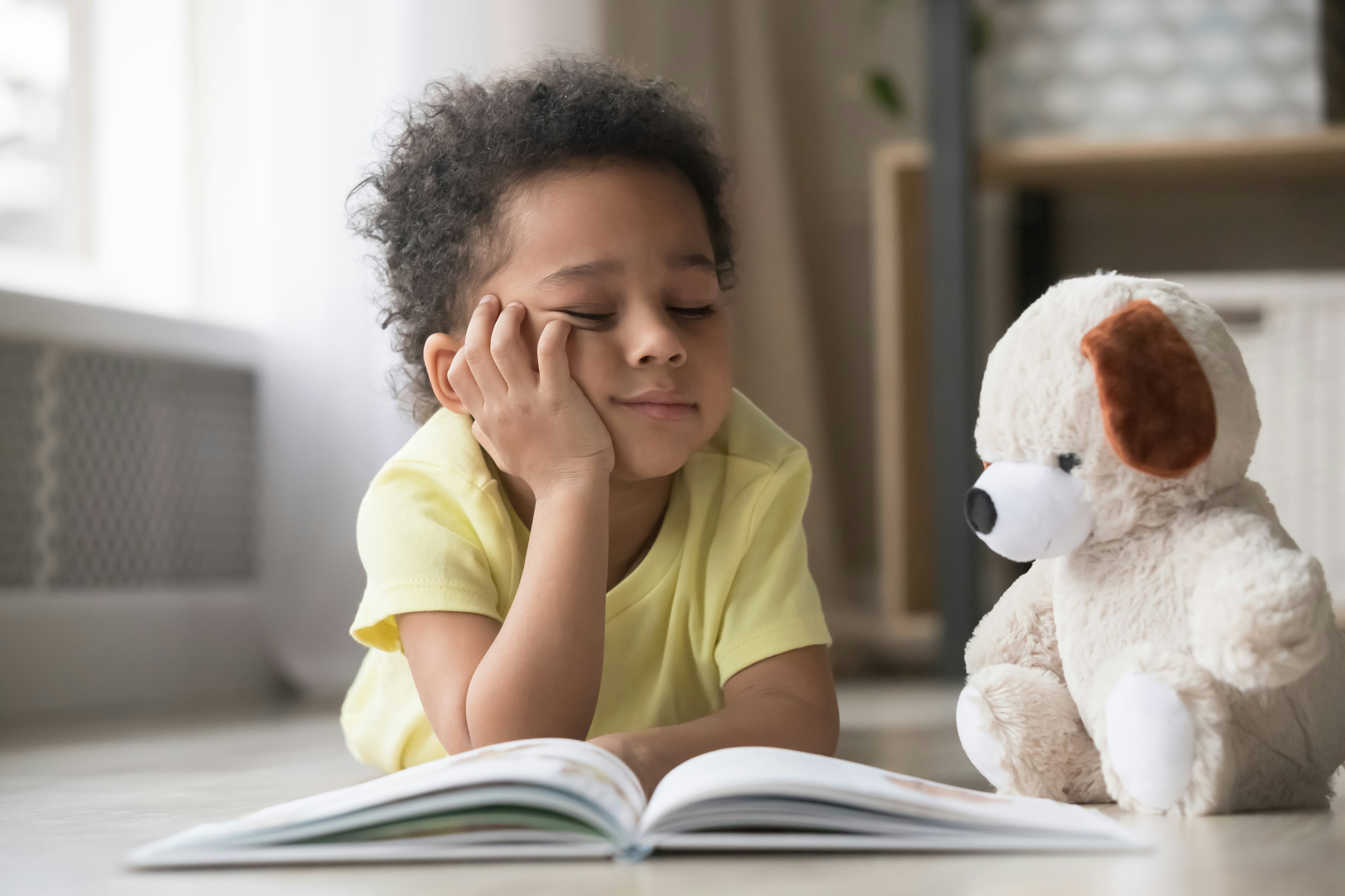 little boy reading a book with his teddy bear