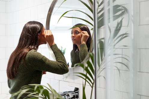 Businesswoman At Home Putting On Make Up In Mirror Before Leaving For Work