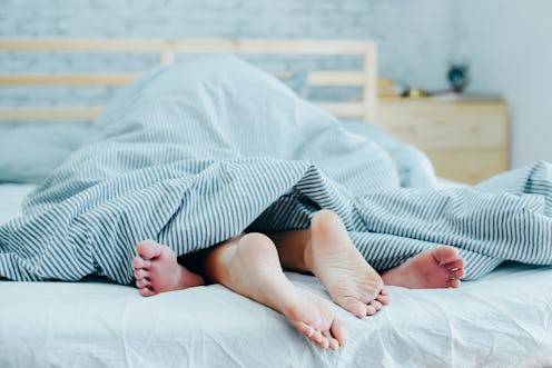 Feet of lovers couple lying on bed under blanket